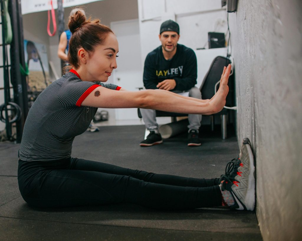 Woman stretching in a gym setting under trainer's guidance, focusing on flexibility and fitness.
